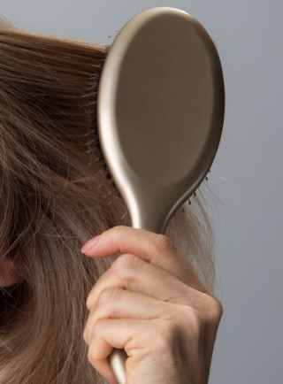 Mujer desenredando su cabello rubio con un cepillo dorado