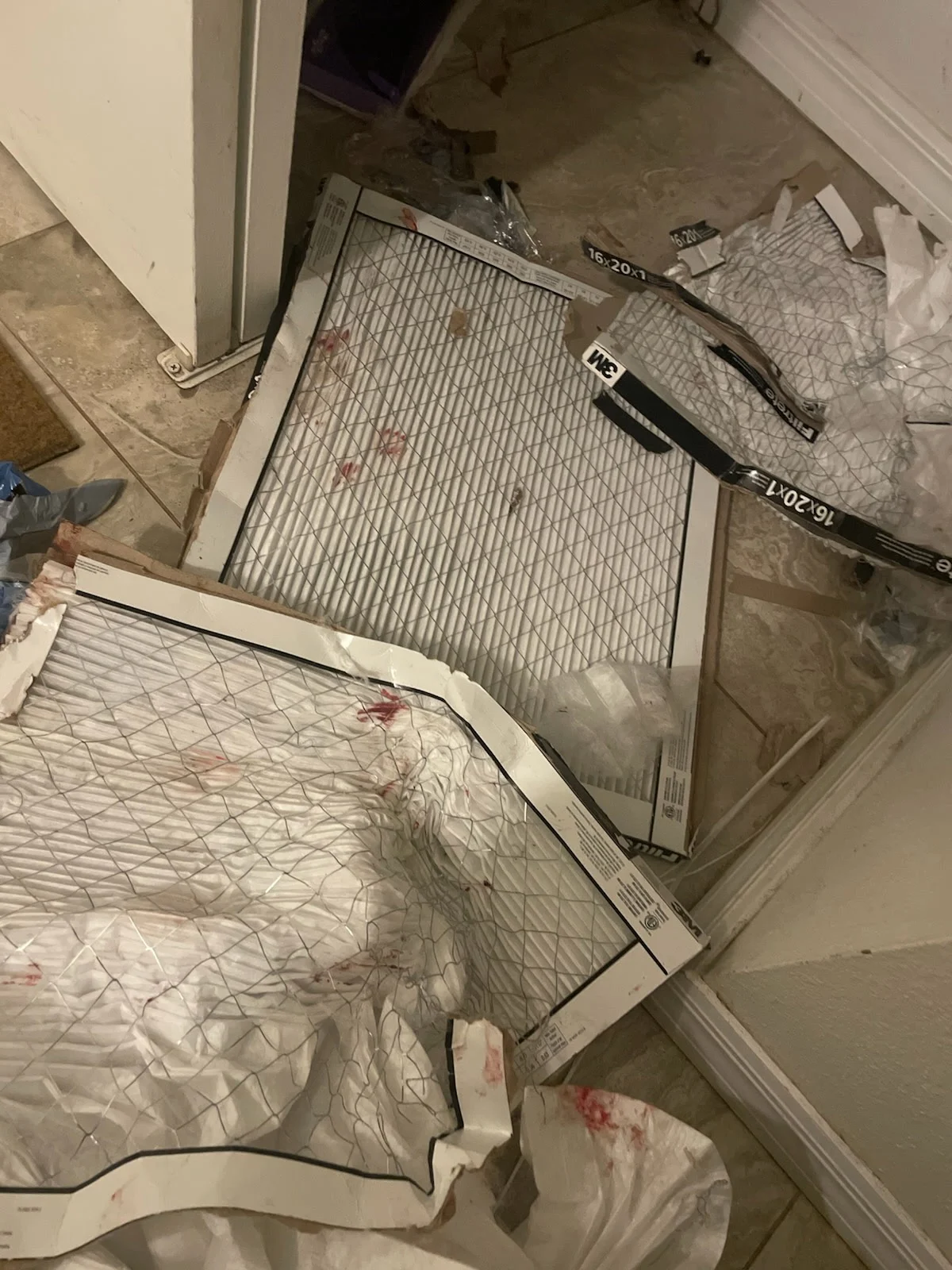 Panting dog with anxious body language by a destroyed door and air filters damaged by the same dog.