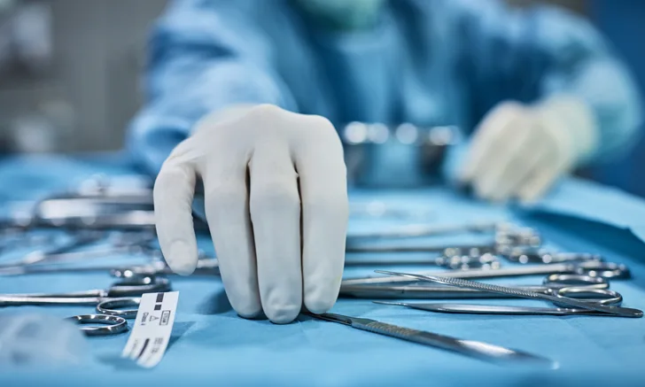 A gloved hand reaching for a surgical tool.