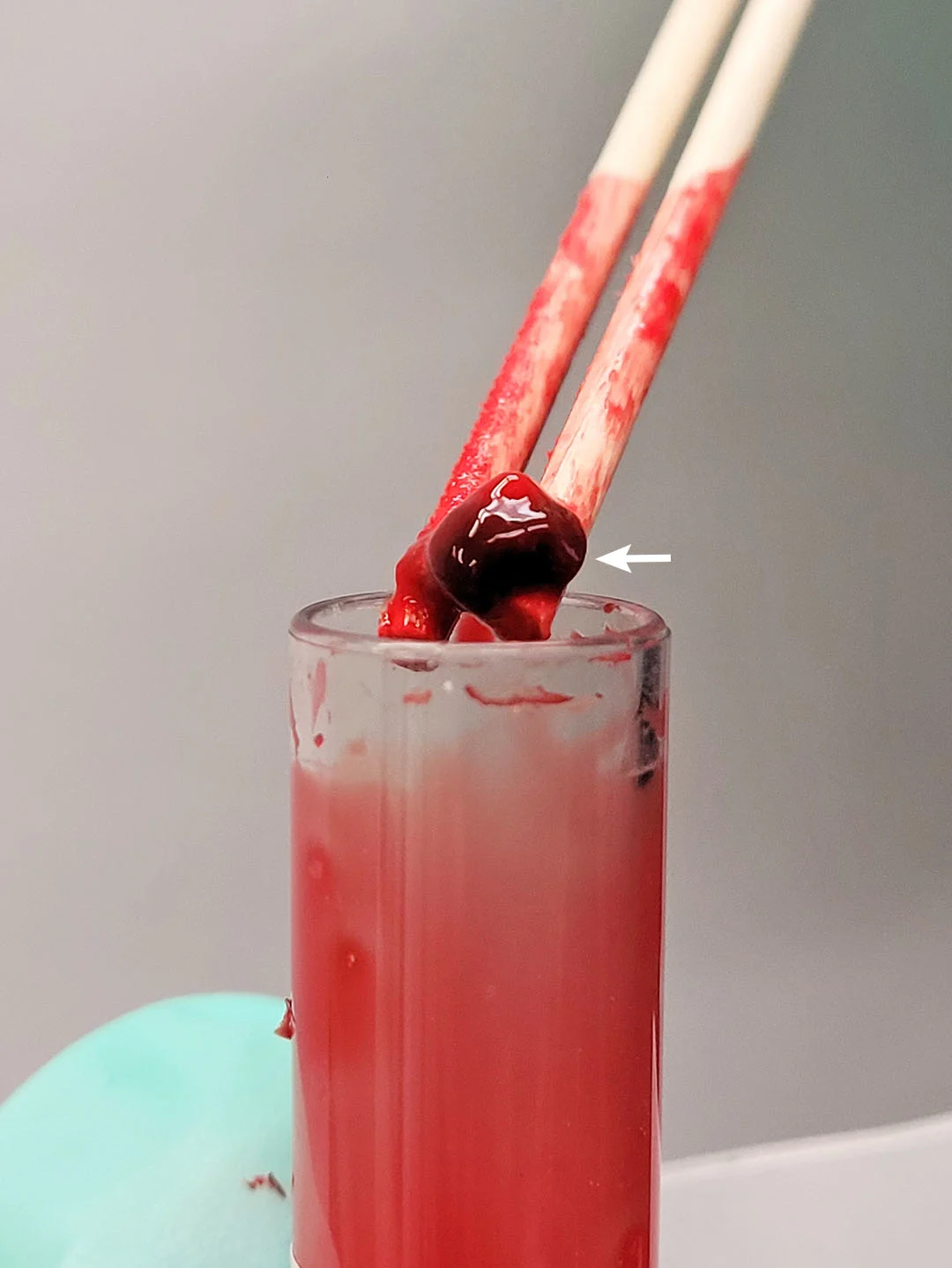 Close-up of two wooden sticks holding large blood clot over top of opened glass blood tube.