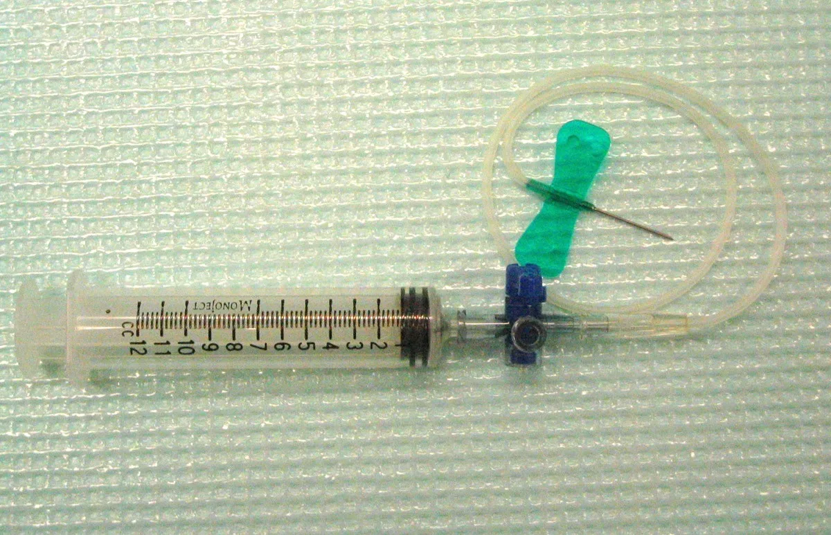 A 12-cc syringe connected to an uncapped butterfly catheter with green wings via a 3-way stopcock.