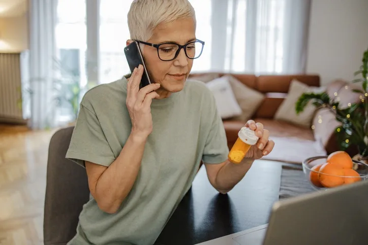 Client holding an unlabeled orange pill bottle while on the phone. 