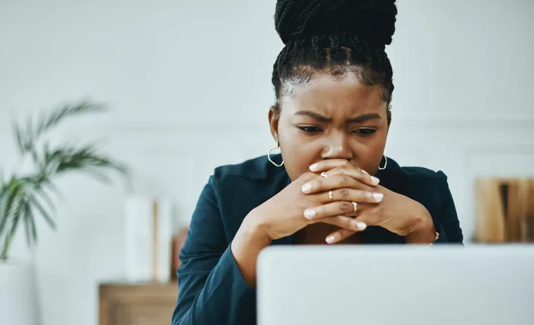A person sitting at a desk, staring at a laptop screen, with a concerned expression on her face.