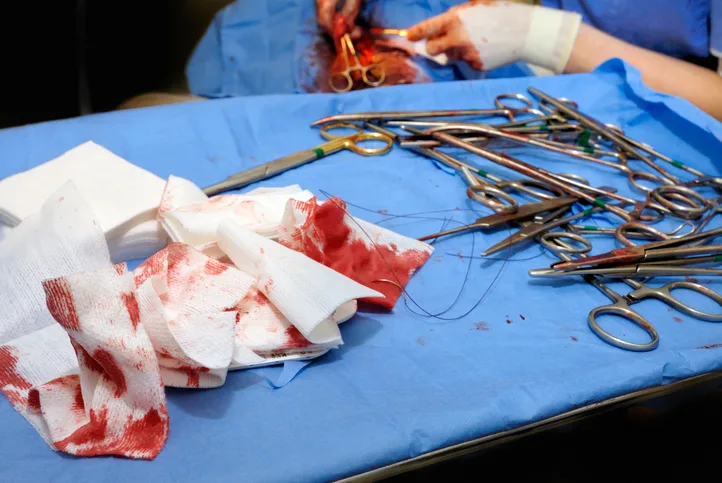 Bloody gauze and instruments on a tray with a spay surgery being performed in the background.