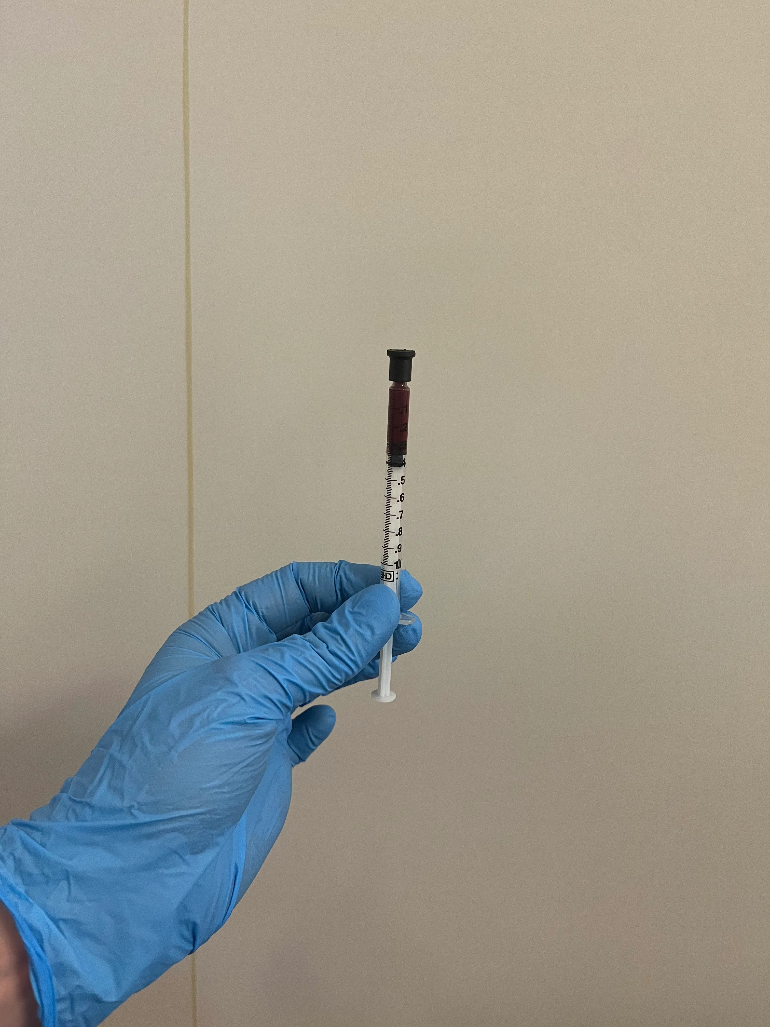 A capped syringe held by a gloved hand.