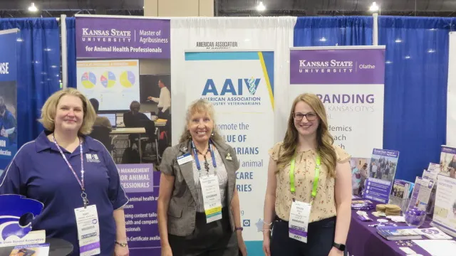 Three people smiling while posing in front of an exhibit booth.