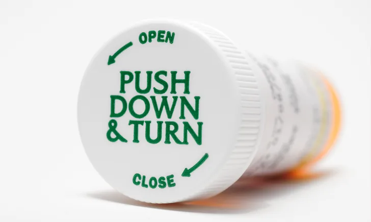 Orange pill container laying on its side, showcasing the top of the bottle. 