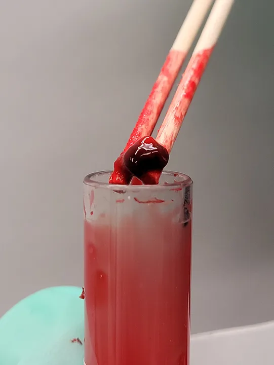 Two wooden sticks shown holding a blood clot above a glass tube.