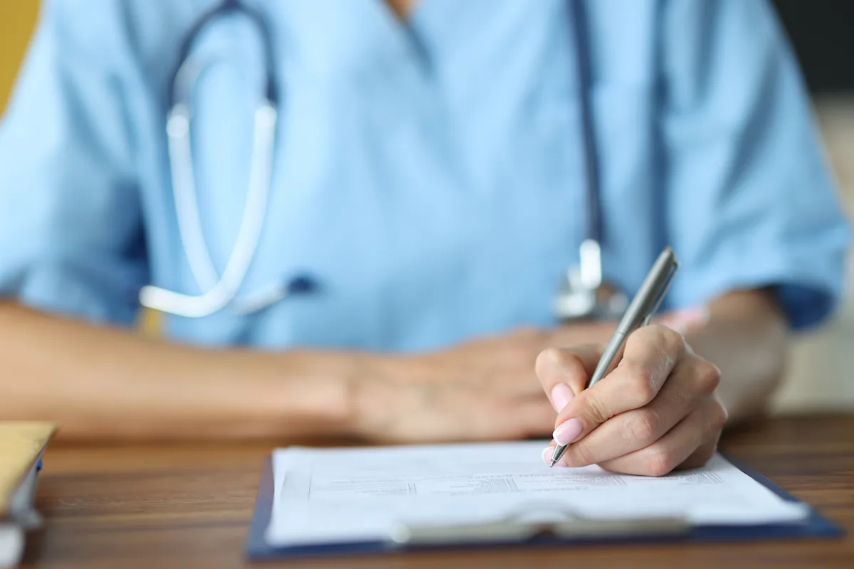 A veterinary professional in blue scrubs filling out a form with a pen.