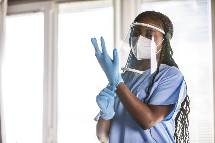 Person wearing face mask and face shield donning examination gloves.