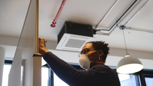 A Person Wearing an N95 Respirator Mask Writes Thoughtfully on a Whiteboard by Airfocus - 600 x 337