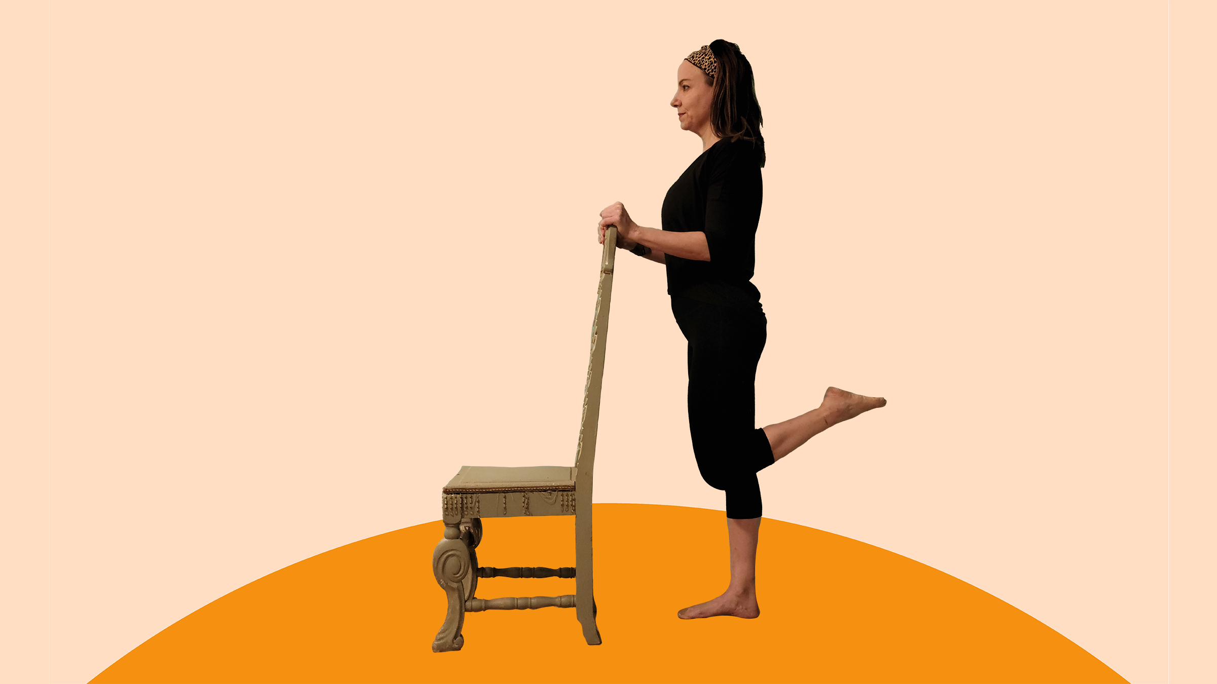 A woman does a standing leg curl chair exercise while holding the back of a chair.