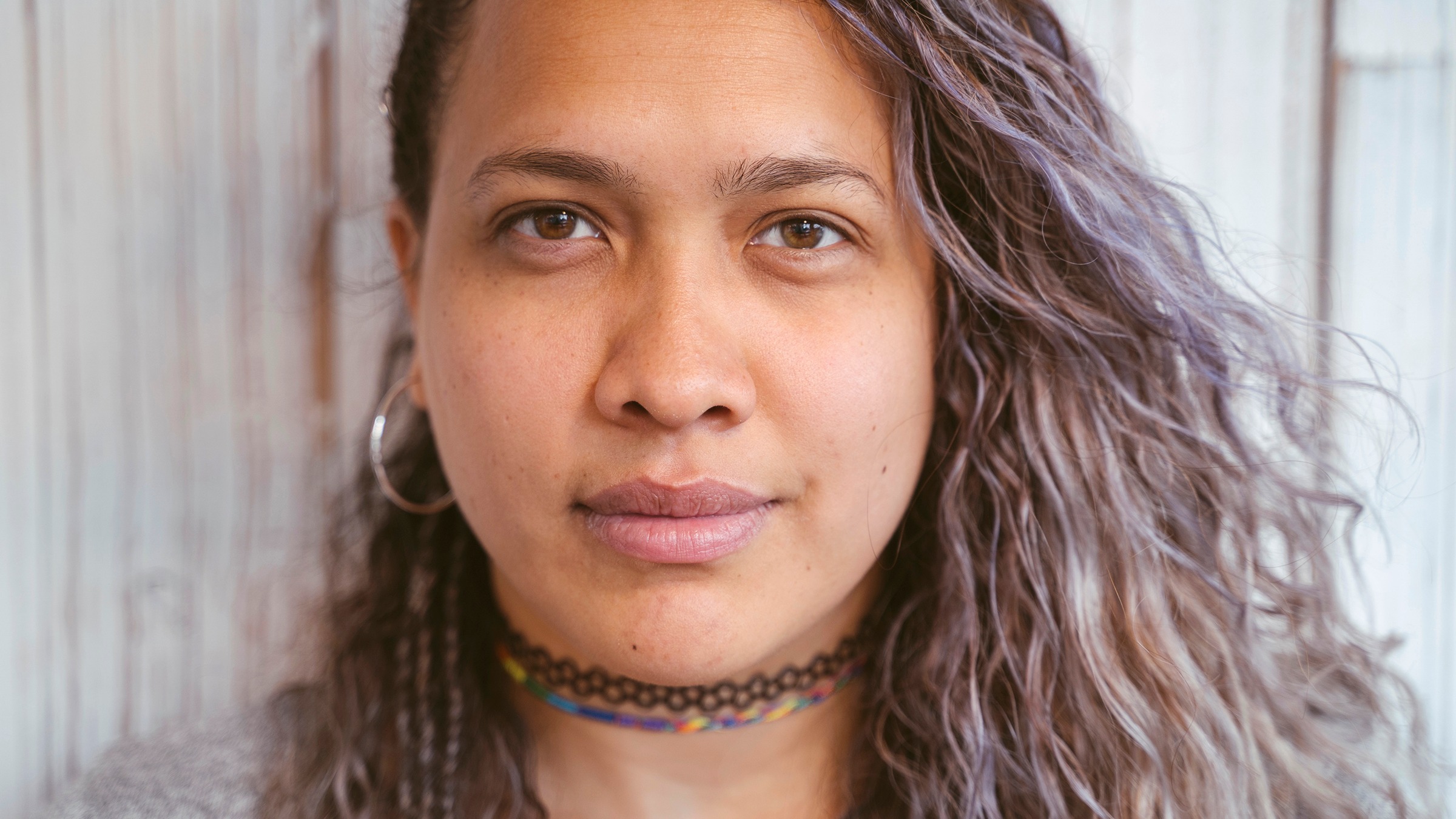 Close-up portrait of a young woman with curly purple gray-ish hair. She is wearing a black choker necklace and has a slight smile on her face.
Beavera/iStock via Getty Images
