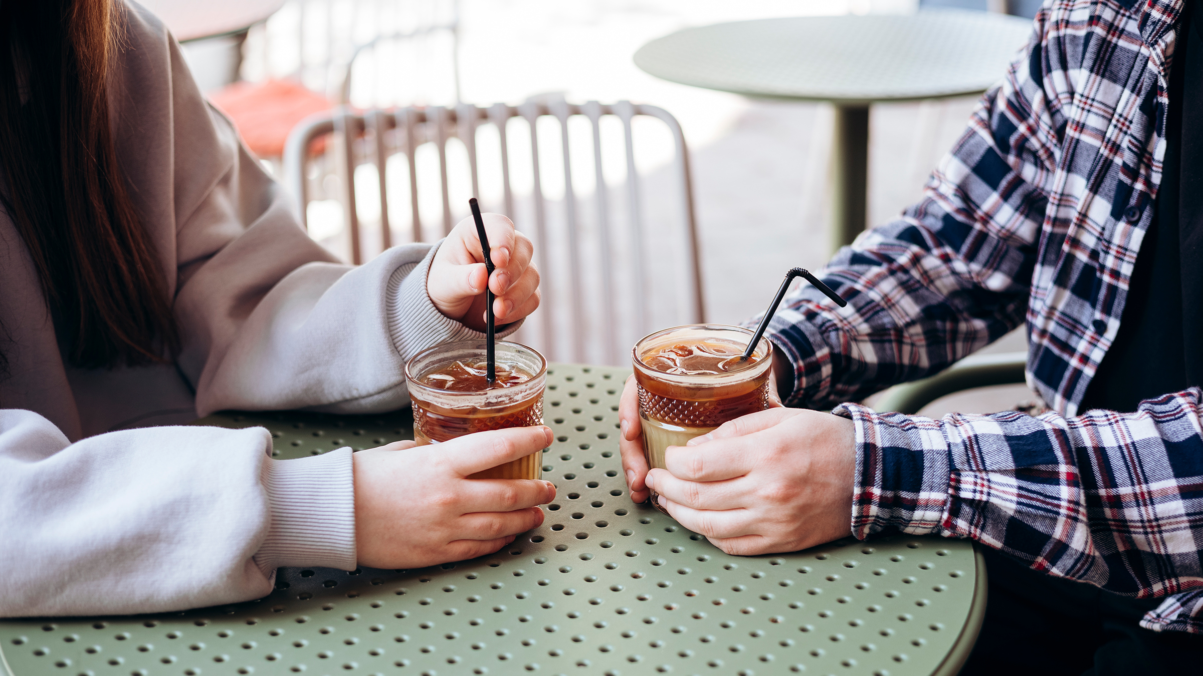 Two people holding iced coffee drinks outdoors, focus on hands and glasses