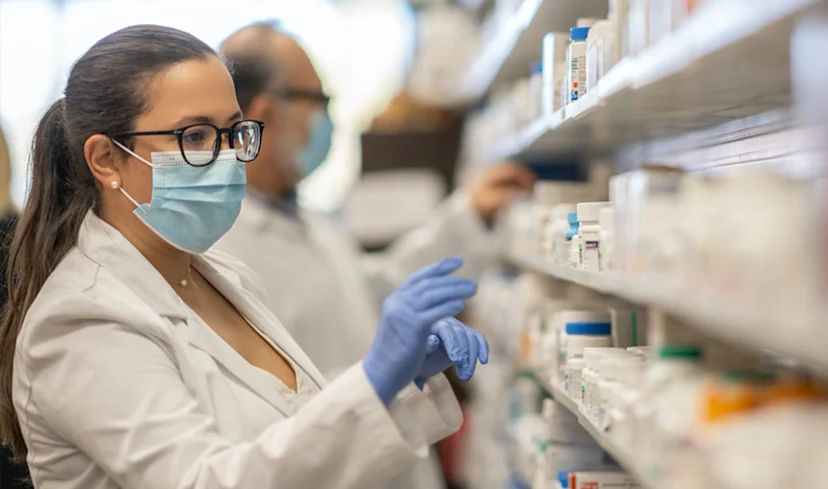 Pharmacist with a mask on looking at a shelf at the pharmacy