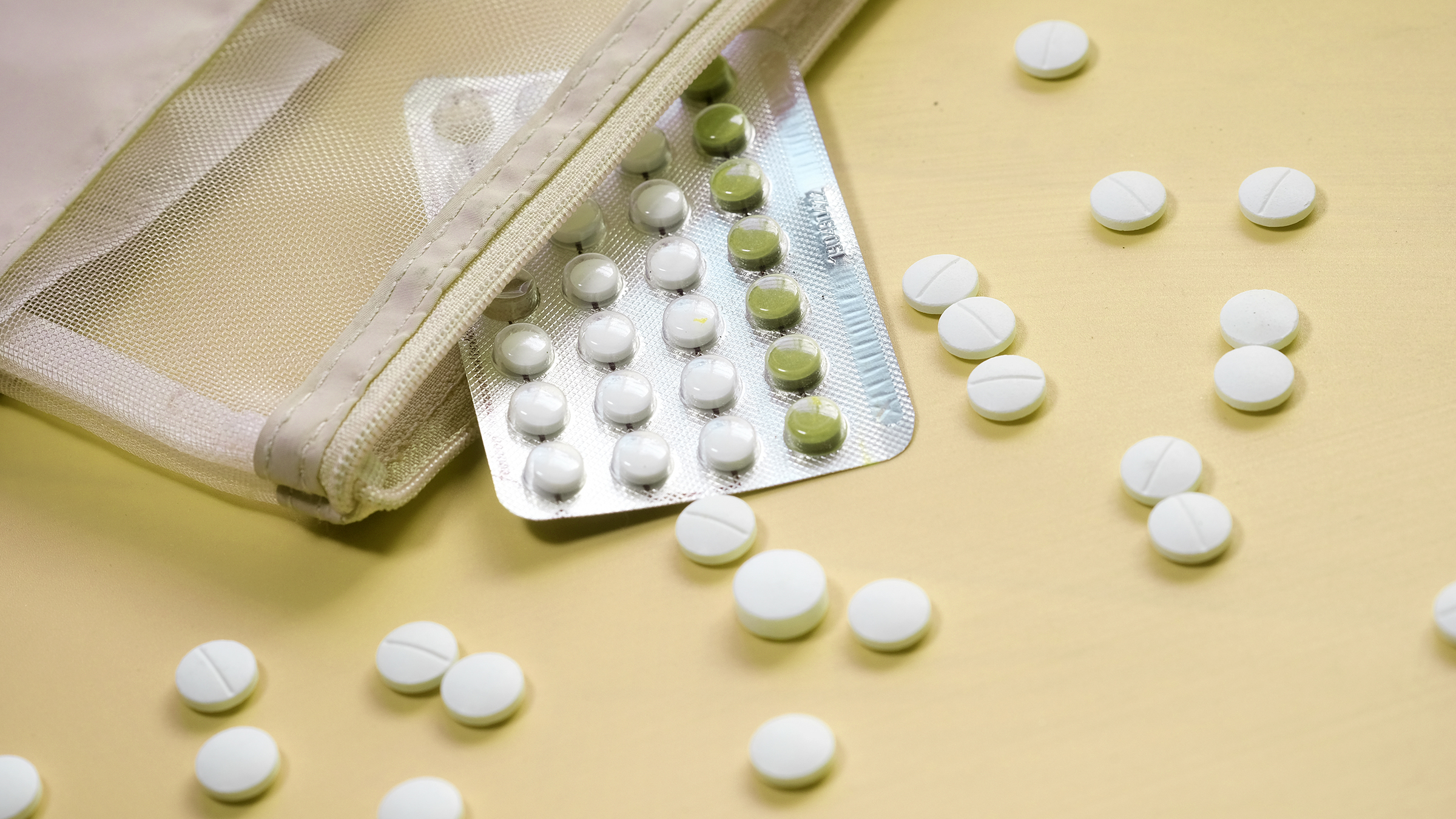 Birth control pills scattered around a pill pack that is in a mesh carrying pouch. The background is light yellow.
towfiqu ahamed/iStock via Getty Images