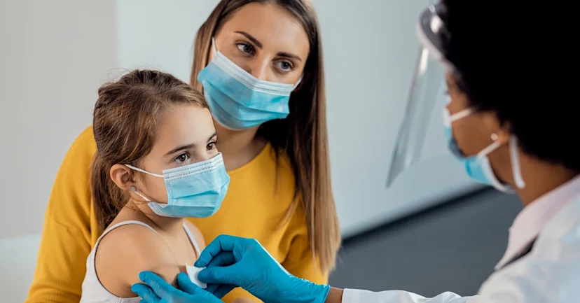 Little girl getting vaccinated by doctor, sitting on mom's lap.