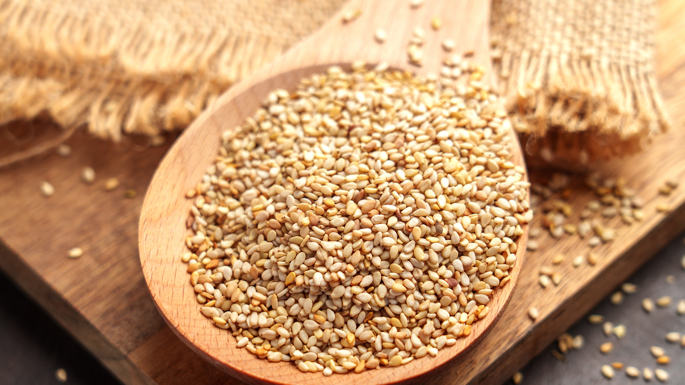 wooden spoon overflowing with pale golden sesame seeds on a cutting board