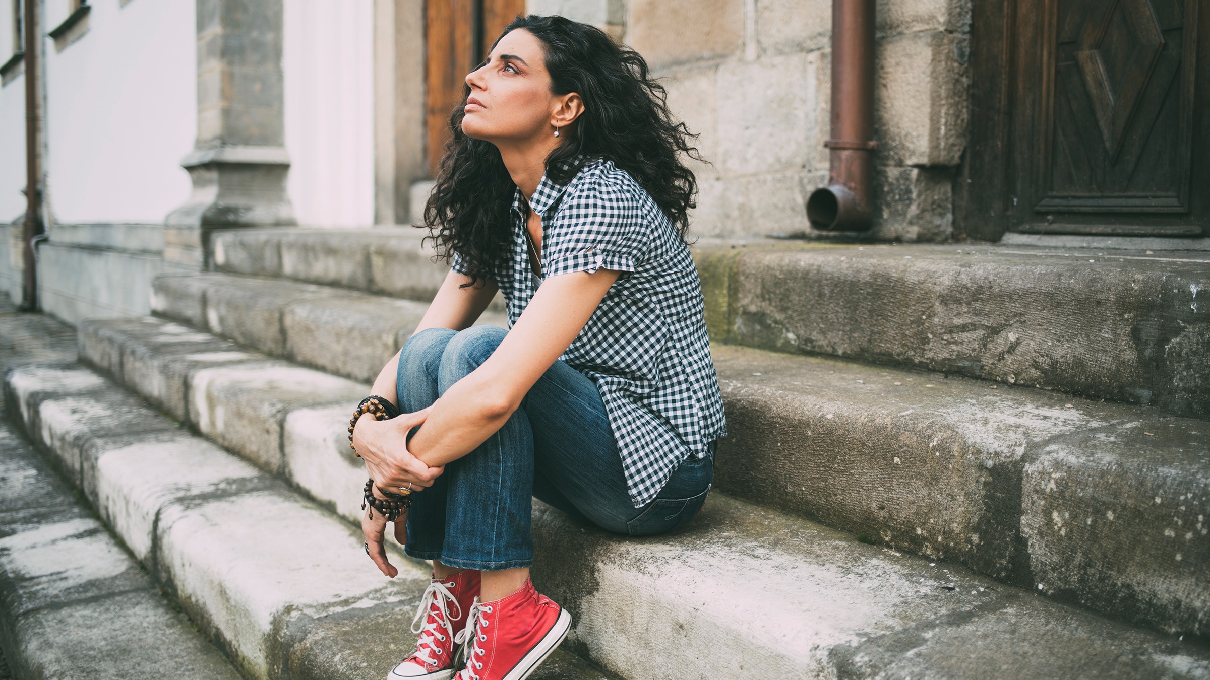  A young woman sits on the steps of a building, looking up in thought with a pensive expression on her face, contemplating her options for medications for treating social anxiety.