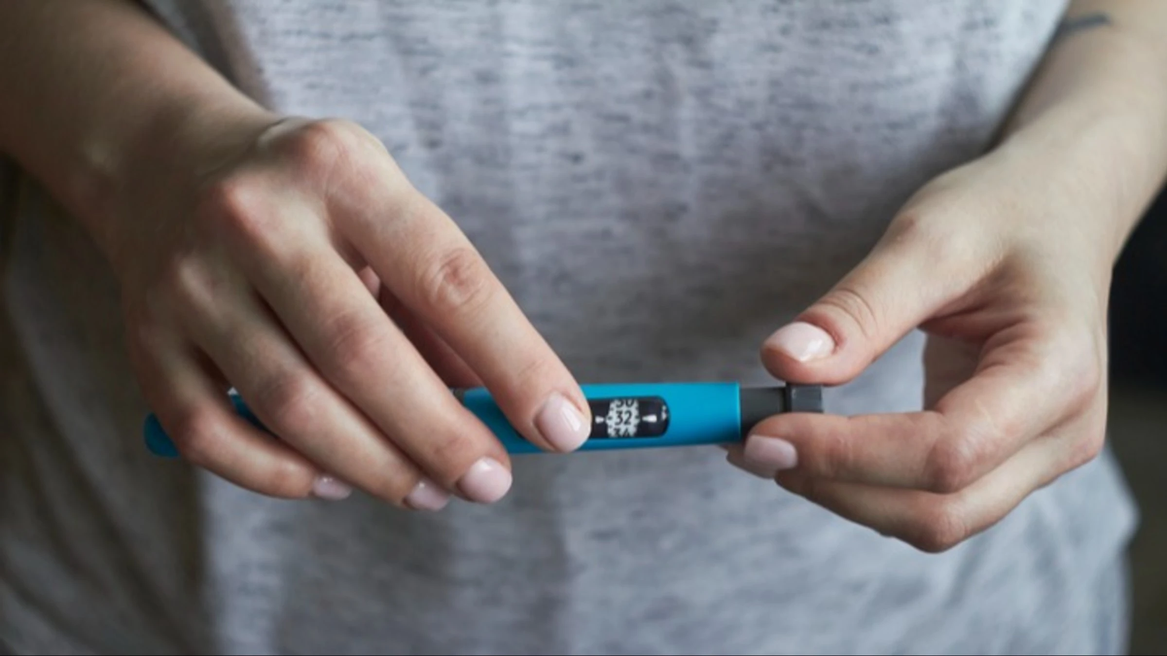 Close-up of a person's hands holding an insulin pen in front of their body with a gray t-shirt on.
Ramann/iStock via Getty Images
