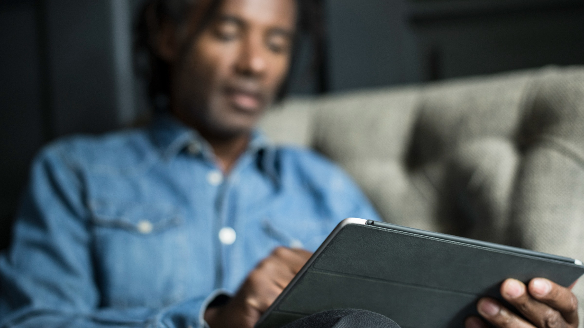 Black man using a tablet as he sits on the couch. His hands and tablet are in focus while he is blurry in the background.
JohnnyGreig/E+ via Getty Image