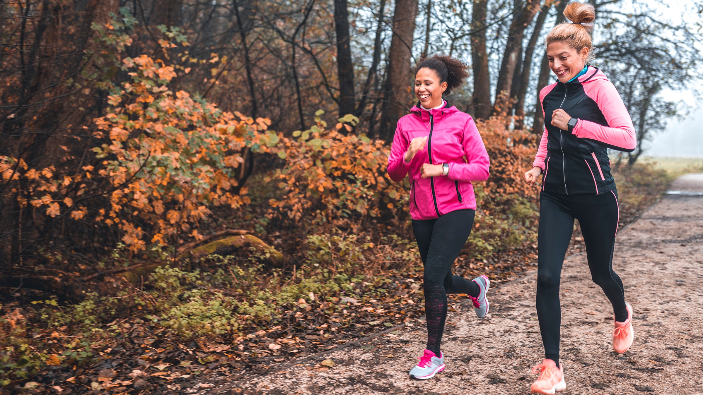 Two women running on a fall day on a park path. They are both wearing pink and black running gear and smiling.
AzmanL/E+ via Getty Images