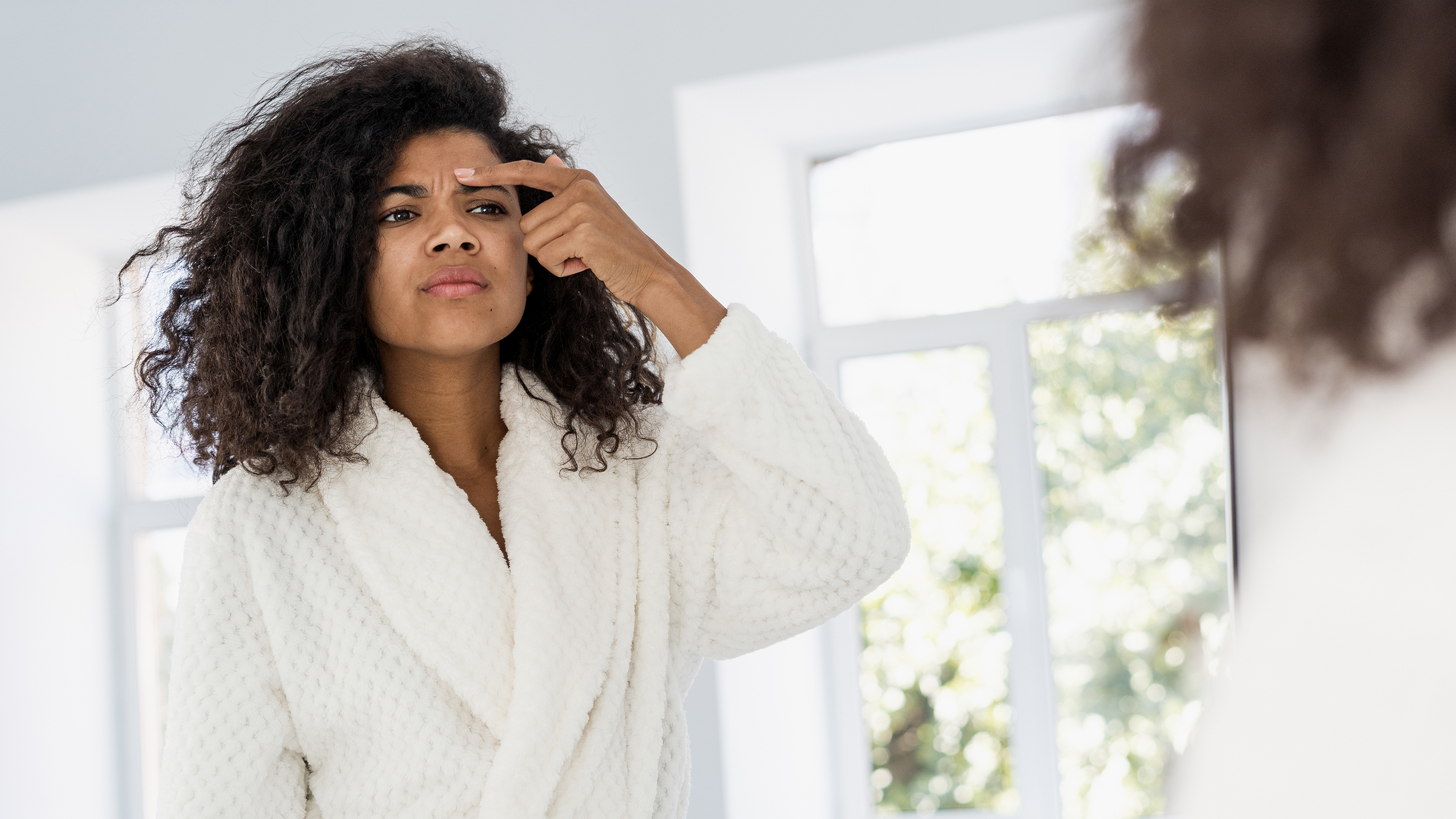Woman looking in the mirror at her skin.
brizmaker/iStock via Getty Images