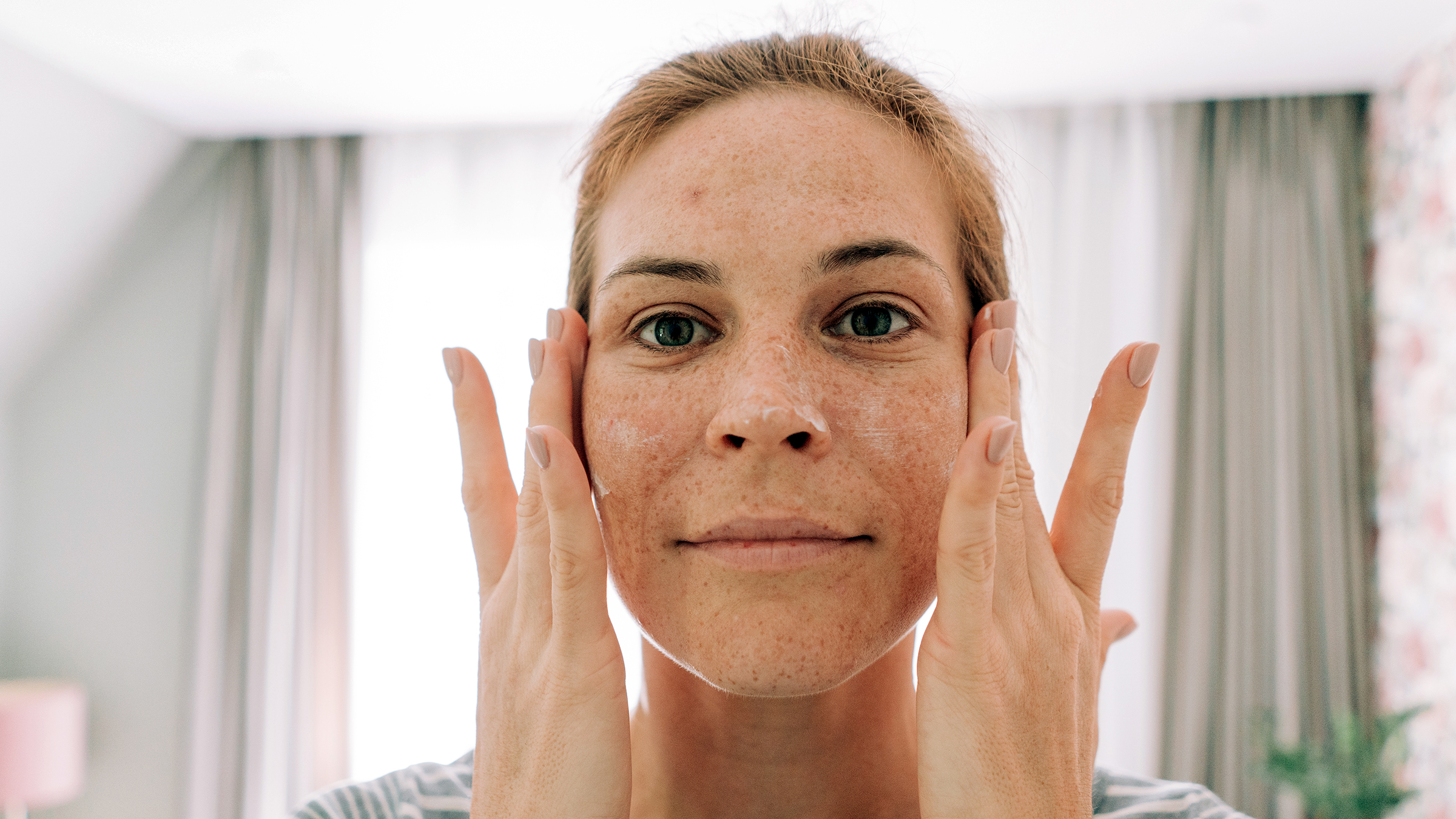 Close-up of a woman applying face cream, showing skincare product on cheeks and forehead