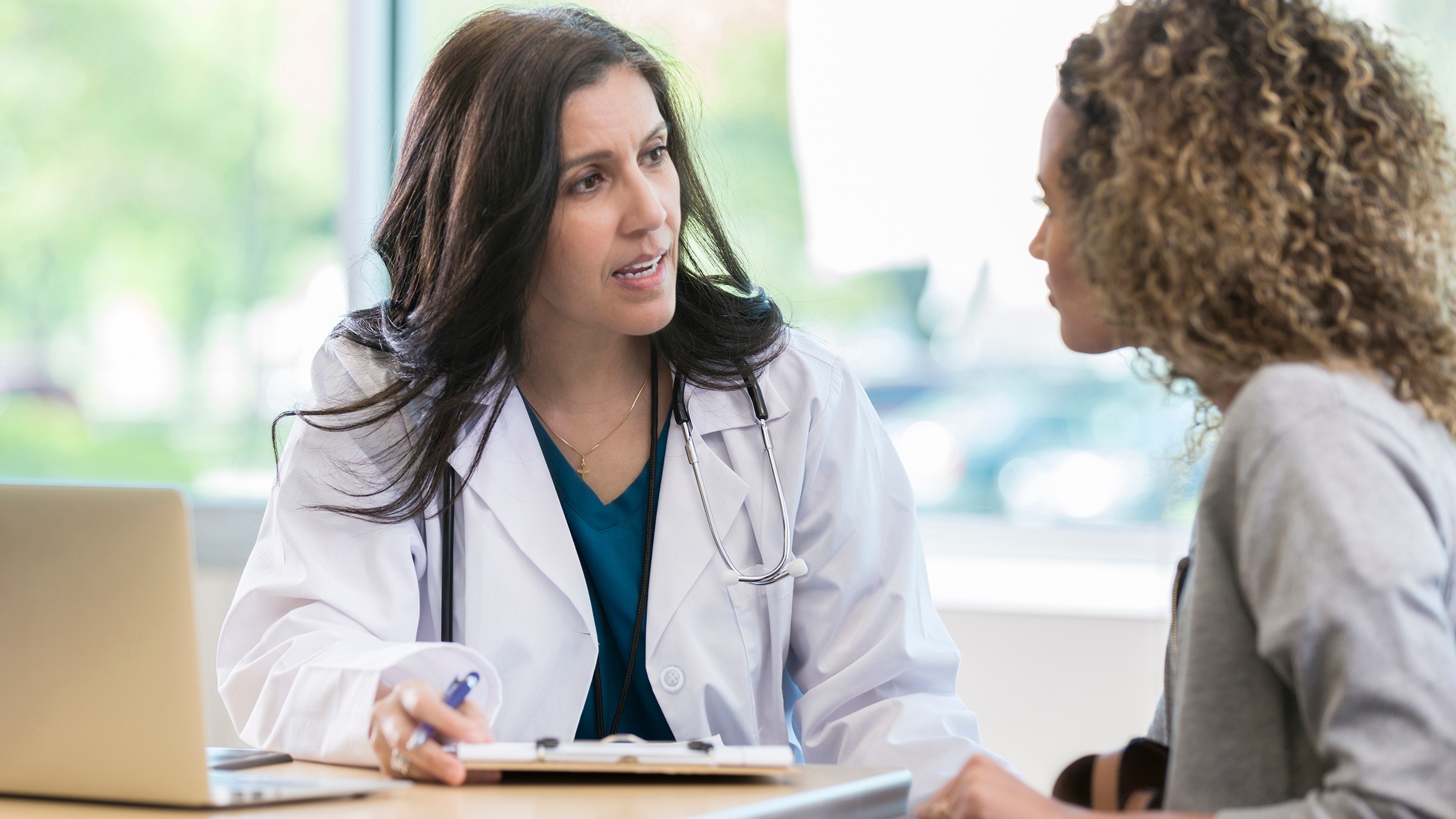 Young woman with curly hair speaking with her doctor. The doctor has a clipboard and pen and is taking notes.
SDI Productions/E+ via Getty Images
