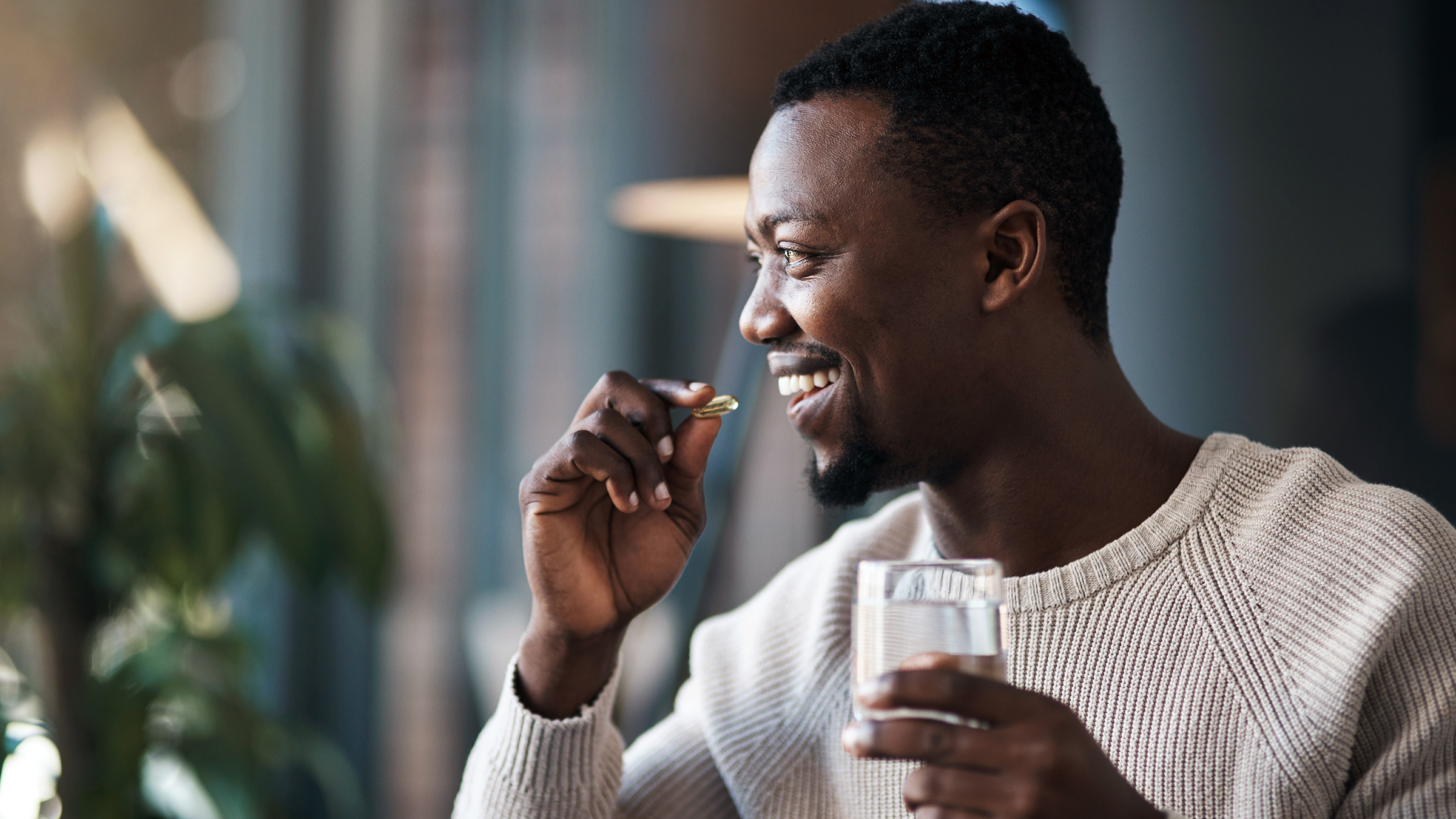A man is taking his medication with water in his living room.
PeopleImages/iStock via Getty Images Plus