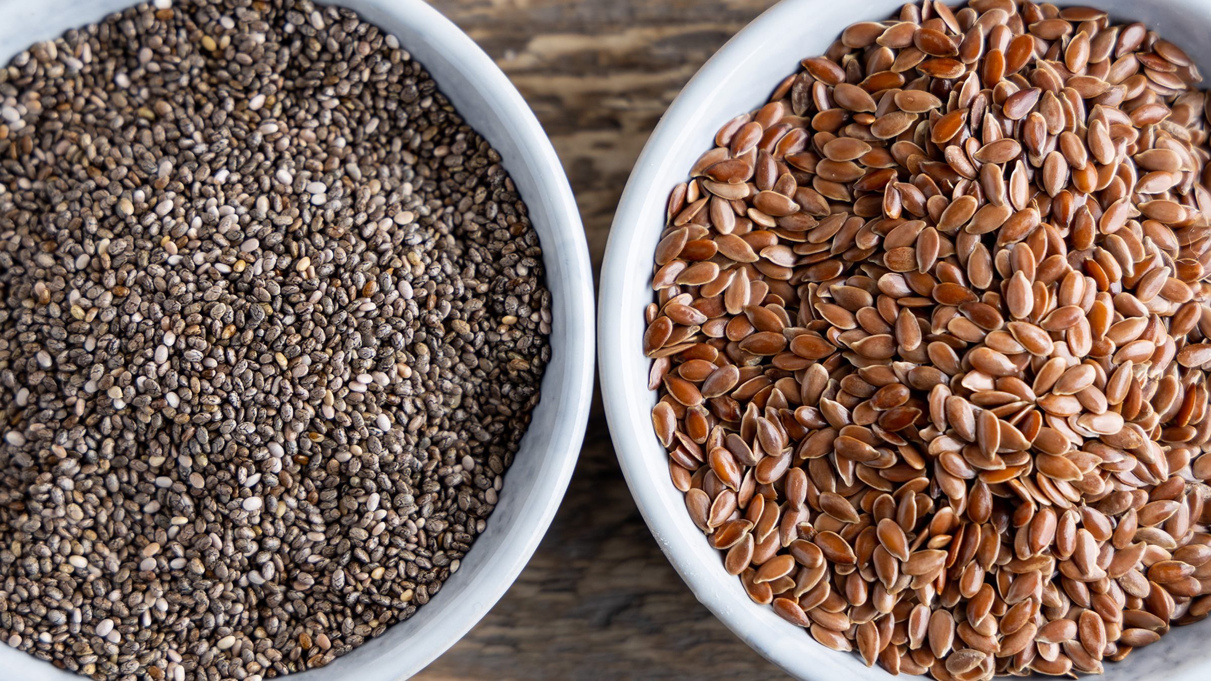 Close-up bowls of chia seeds and flax seeds side by side on a wooden surface