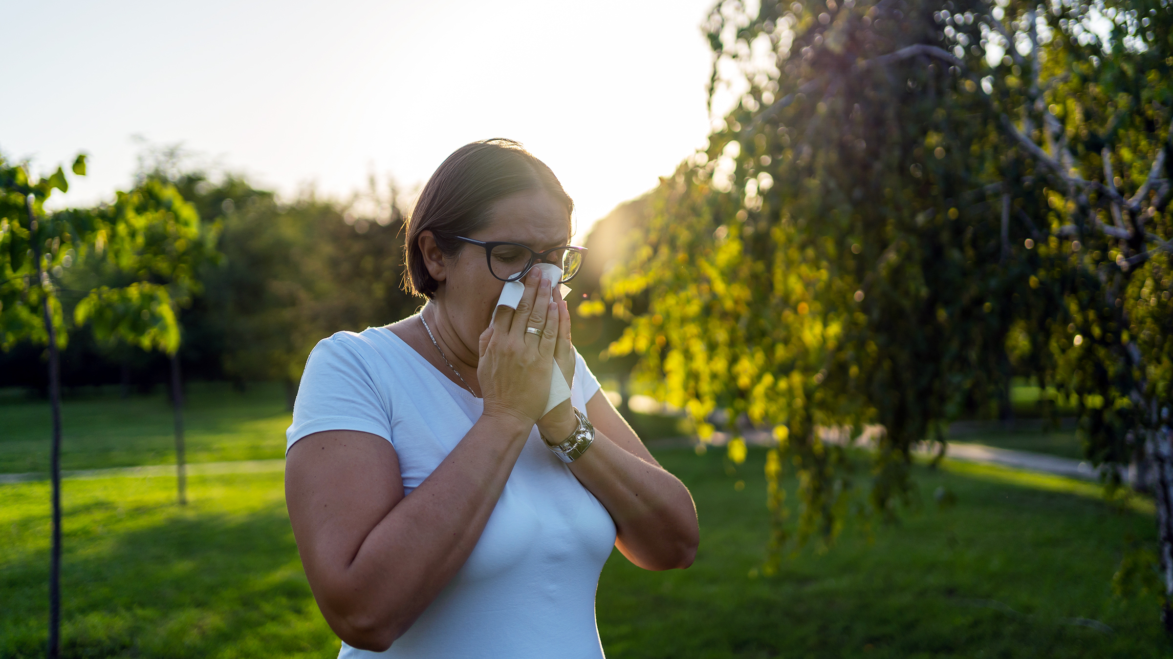 A woman with allergy symptoms blows her nose outside.
Nenad Cavoski/iStock via Getty Images Plus 