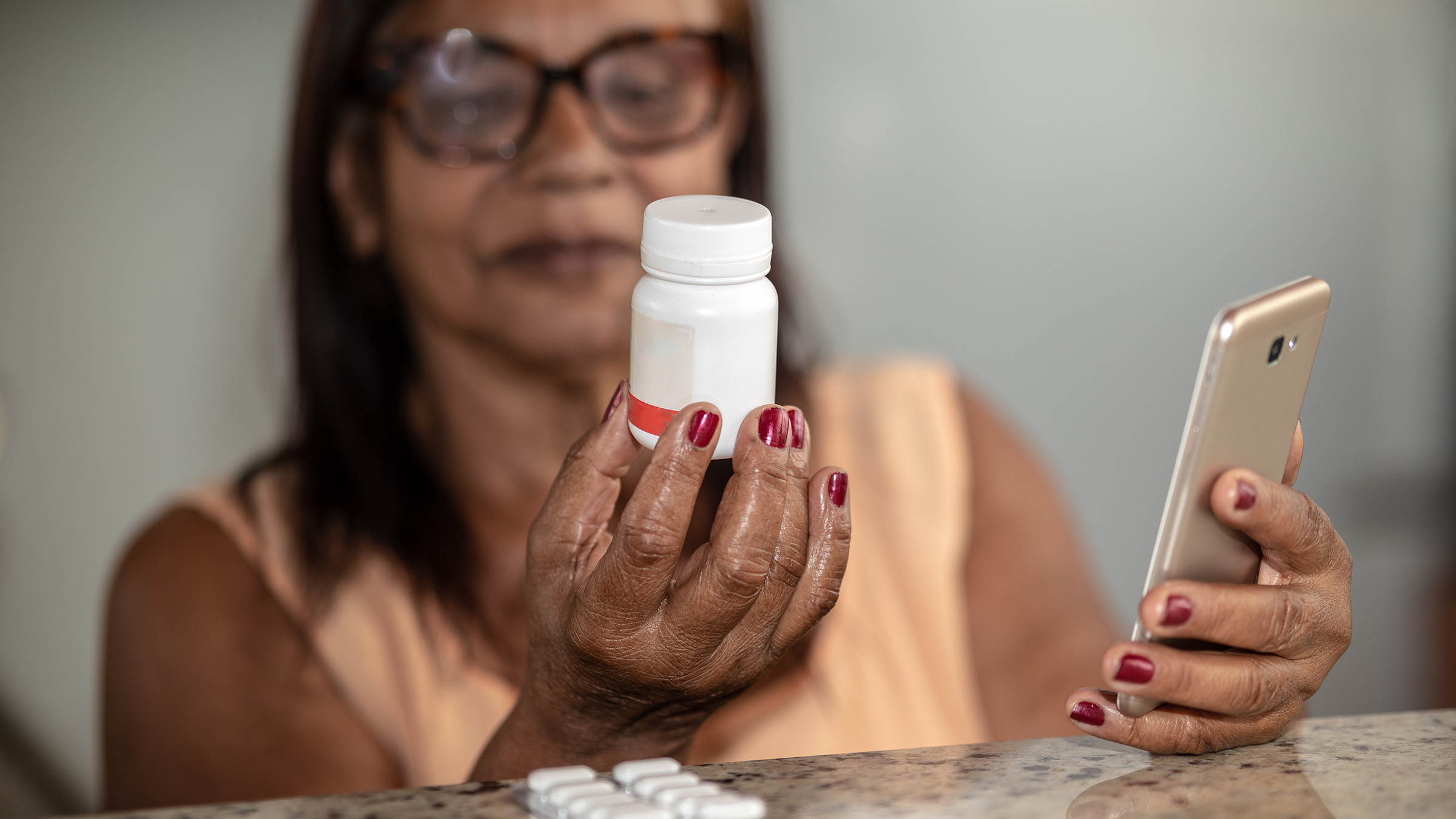 senior woman checking a pill bottle while looking at her smartphone, concerned about medications