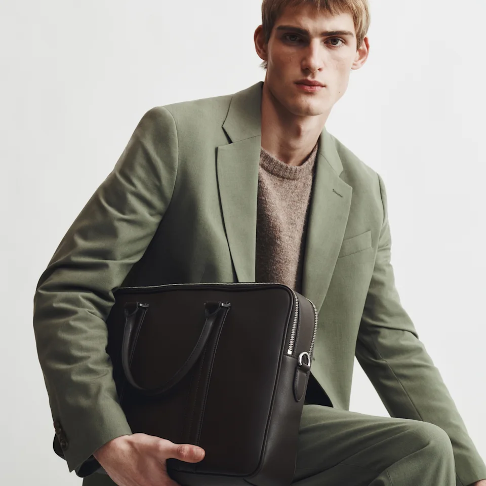 Man in an olive suit holding a dark leather briefcase