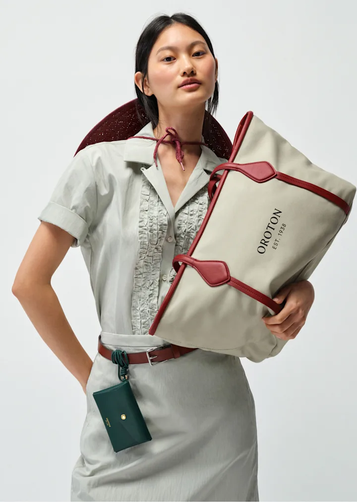 Model in a sage shirt carrying a canvas tote with red trim