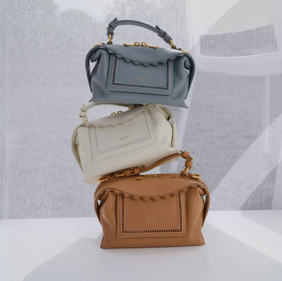 Three Oroton bags in blue, cream and tan stacked on a plinth