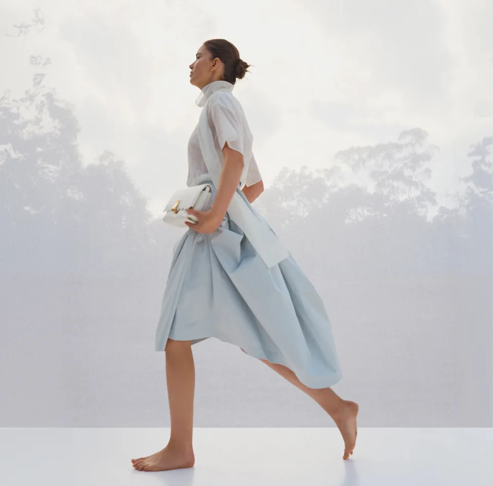 Model in a pale blue shirt and skirt walking barefoot