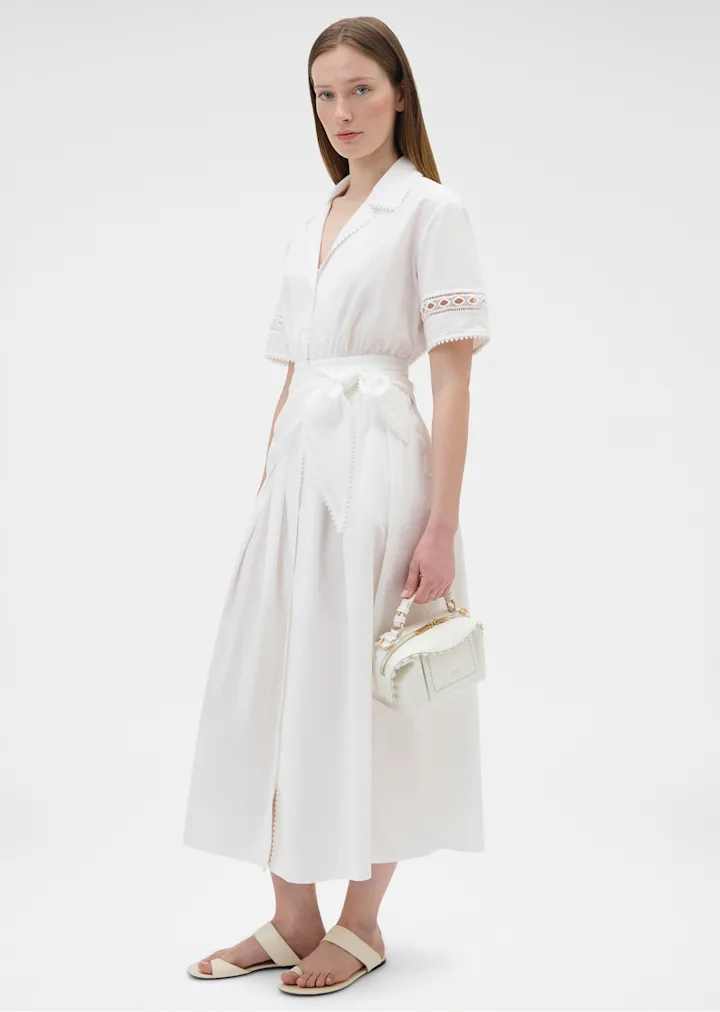 Model in a white shirt dress holding a white leather bag