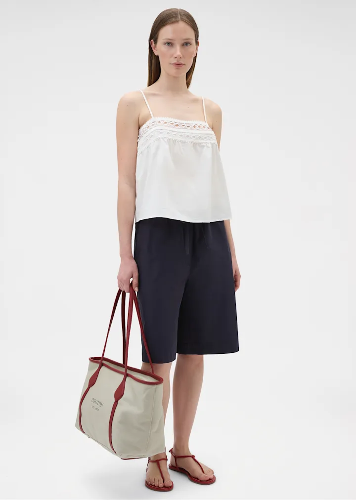 Model in a white lace trim camisole and navy shorts carrying a canvas tote