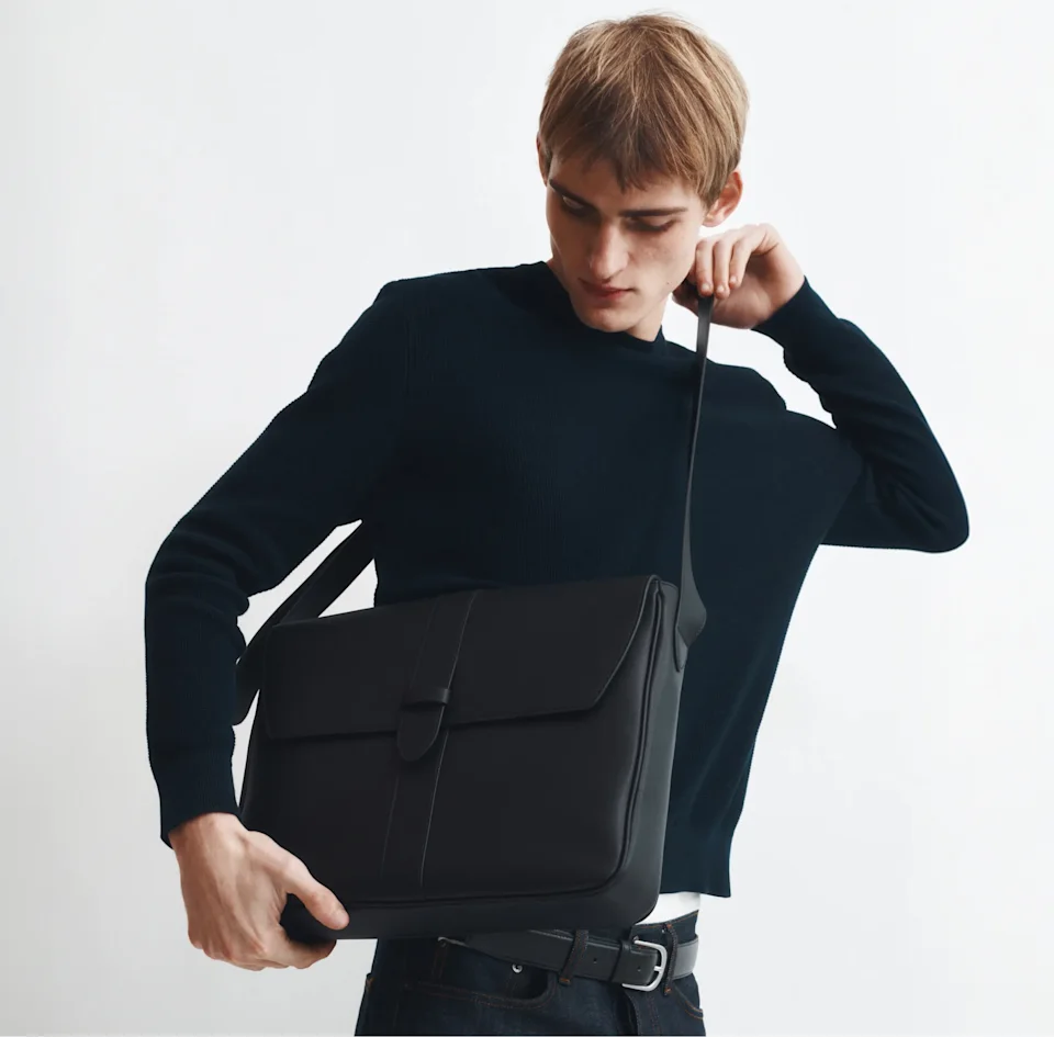 Man in a navy jumper holding a black leather messenger bag