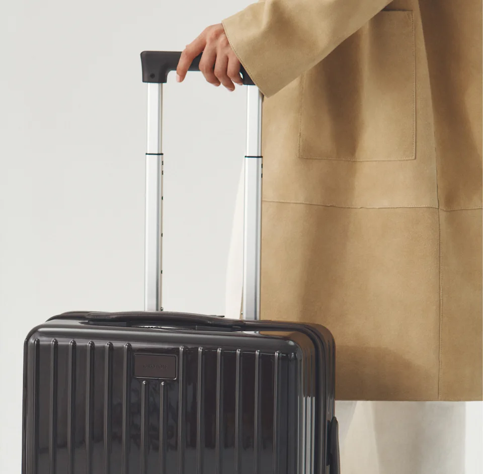 Dark brown Jet Carry On Roller Case pulled by a model in a camel coat
