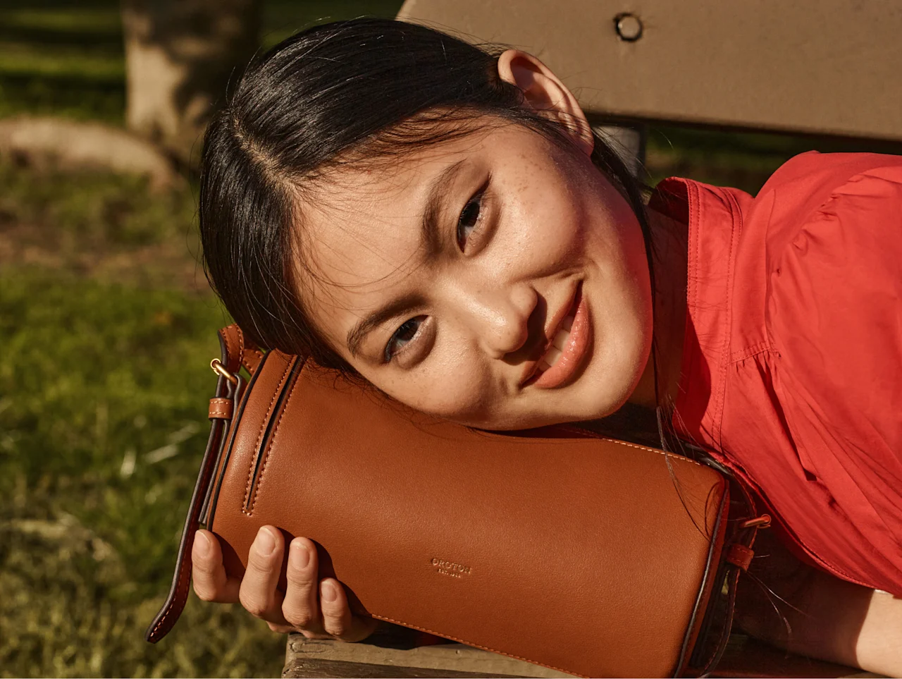 Model resting her cheek on a tan leather Oroton crossbody bag
