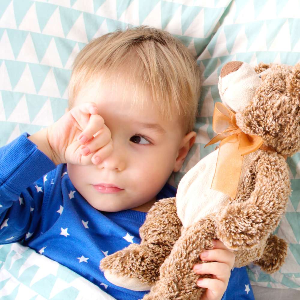 Toddler laying in bed awake holding teddy bear