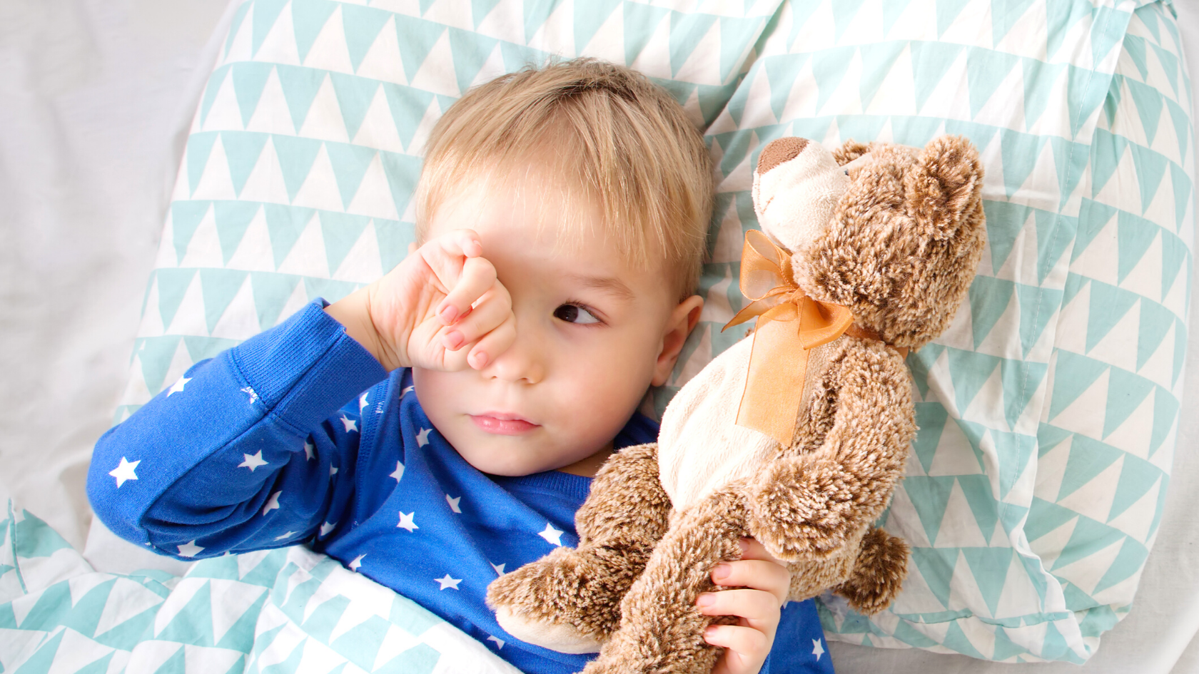 Toddler laying in bed awake holding teddy bear