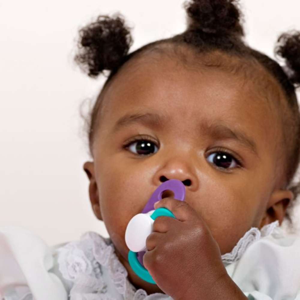 A baby girl is using a pacifier.