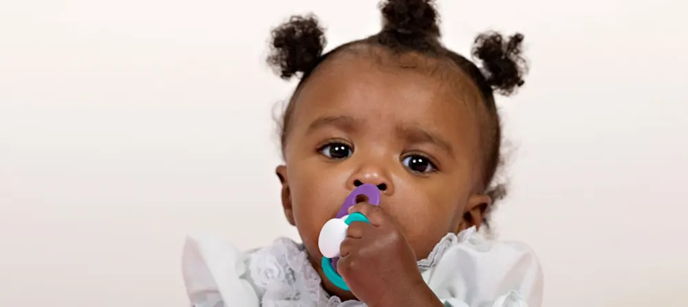 A baby girl is using a pacifier.