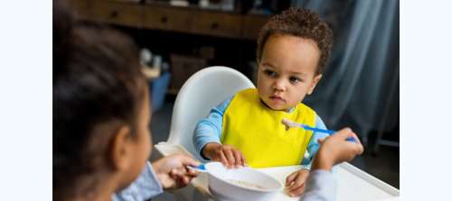 Baby in high chair being fed cereal with a spoon
