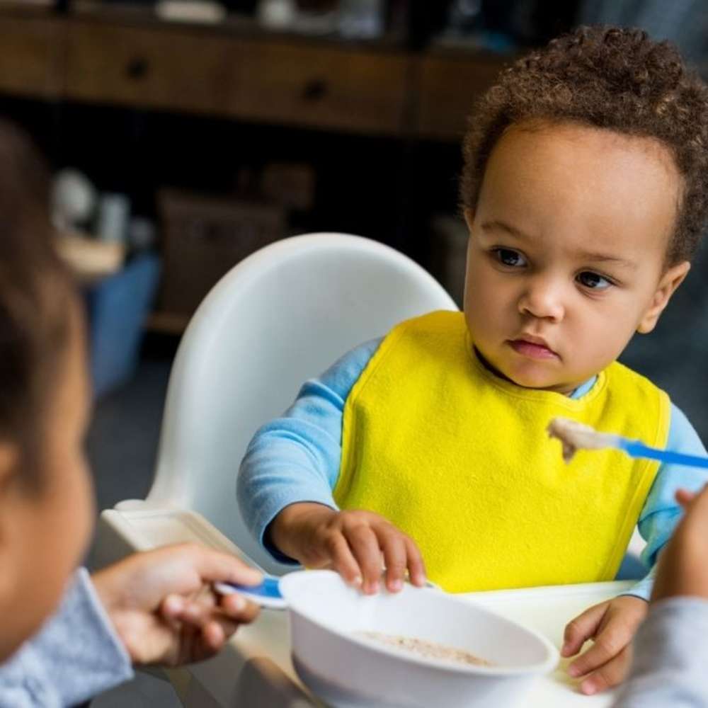 Baby in high chair being fed cereal with a spoon