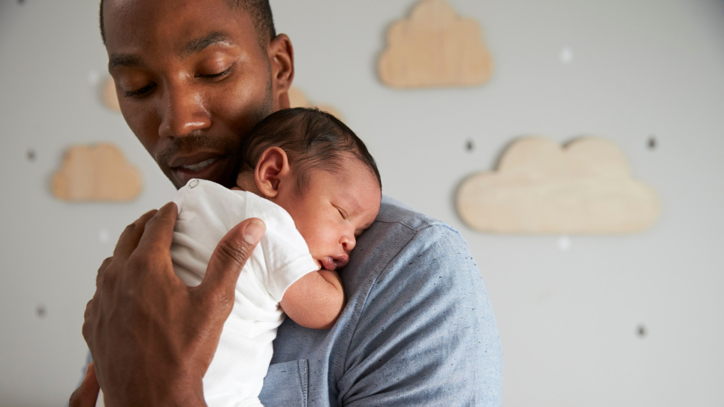 A newborn baby being held up over upper chest and shoulder by Dad as he rocks him to sleep.