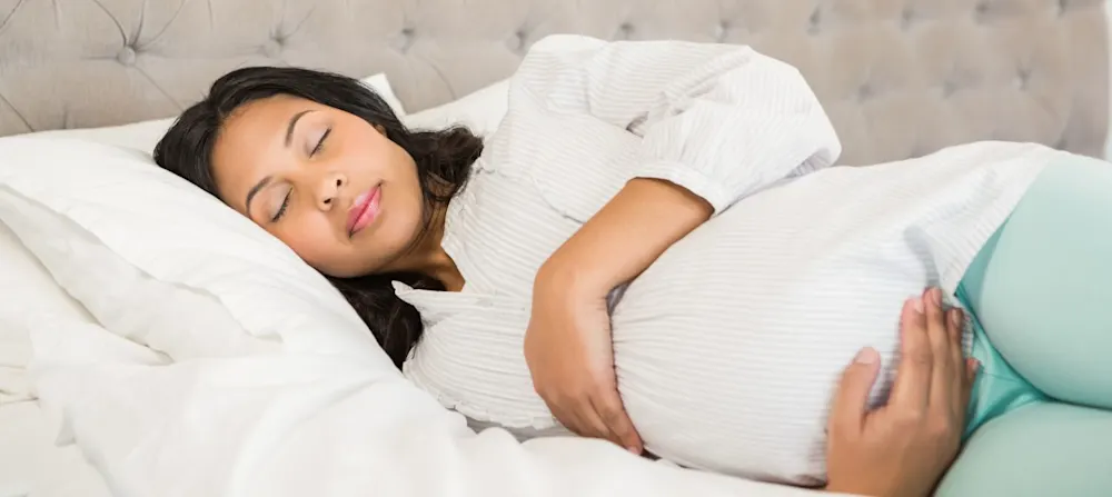 A pregnant woman sleeping on her side, holding her belly.
